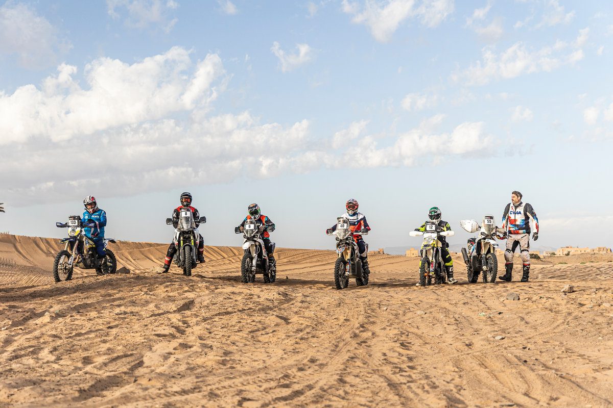 Line of rally motorcycles and riders waiting on open desert ground at Addax Rally